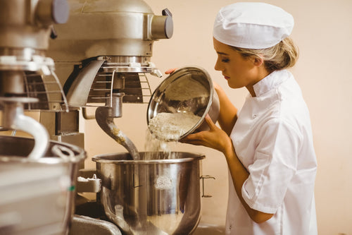 Woman in a white dress adding flour into a spiral mixer